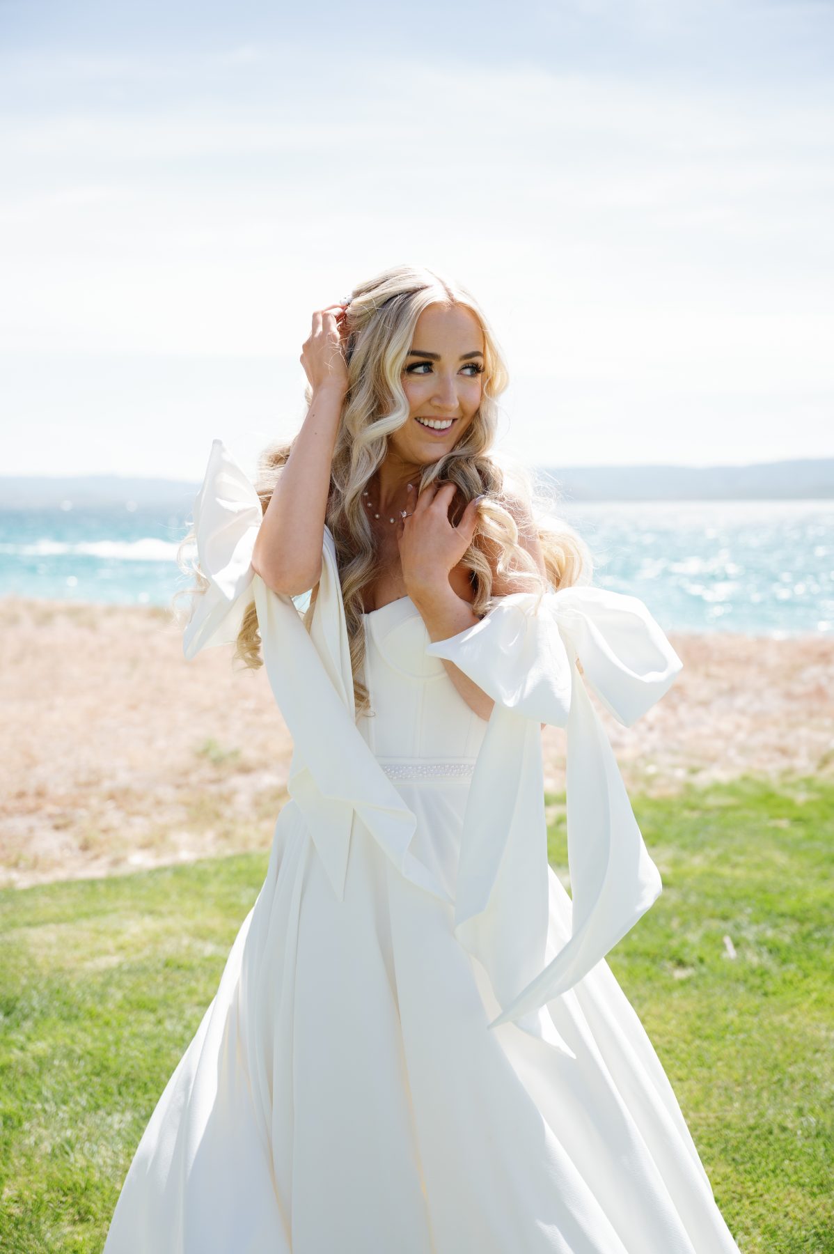 Bride in long blonde waves on a grassy bluff above the ocean