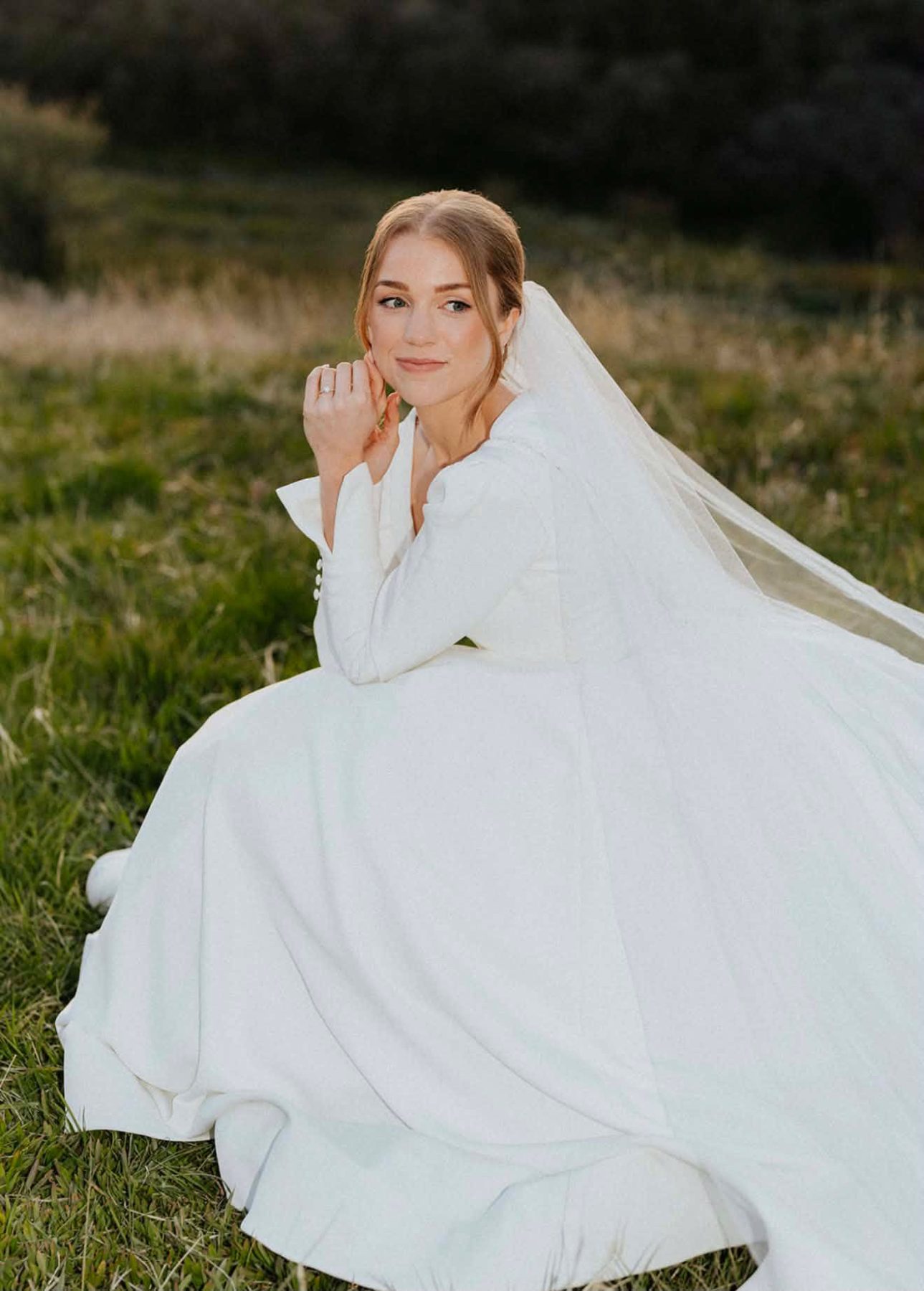 Bride seated in a field wearing a long veil